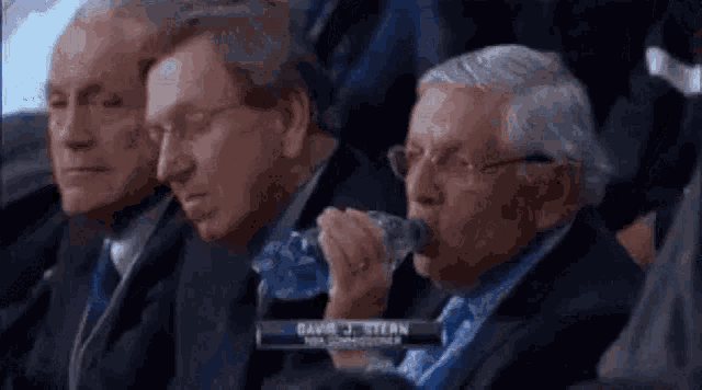 three men are sitting in a row and one is drinking water from a bottle