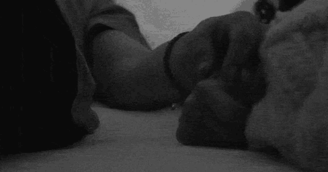 a black and white photo of a person holding another person 's hand while laying on a bed .