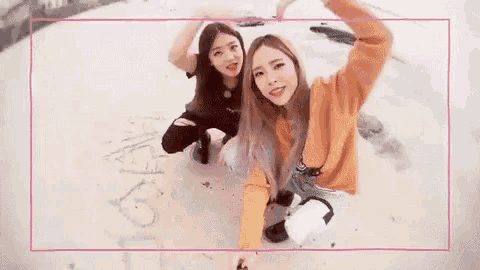two young women are kneeling down on the ground making a heart shape with their hands .