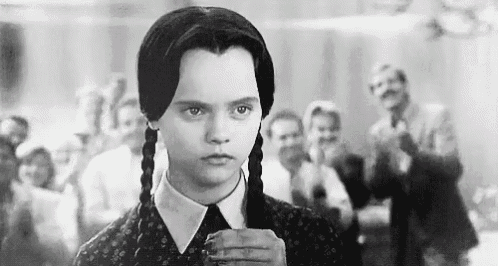 a black and white photo of a girl with pigtails standing in front of a group of people .