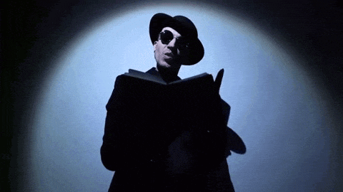 a man in a hat and sunglasses is holding a book in his hand .