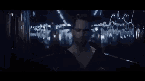 a man with a beard is standing in a dark room with lights reflected in the mirror .
