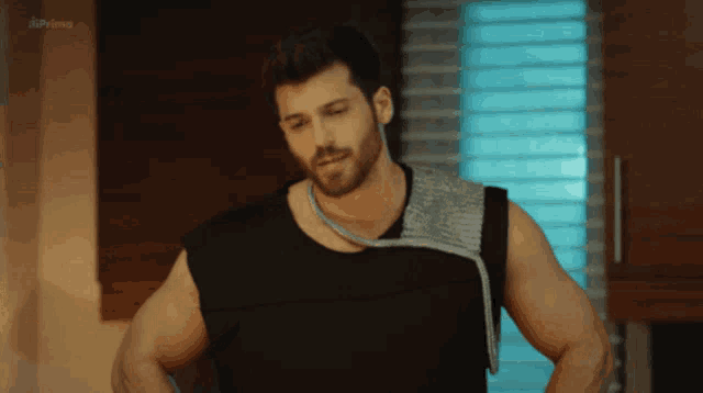 a man wearing a black tank top is standing in front of a window with the word prime on the bottom right
