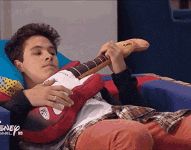 a young man is laying on a bed holding a stuffed guitar with disney channel written on the bottom right