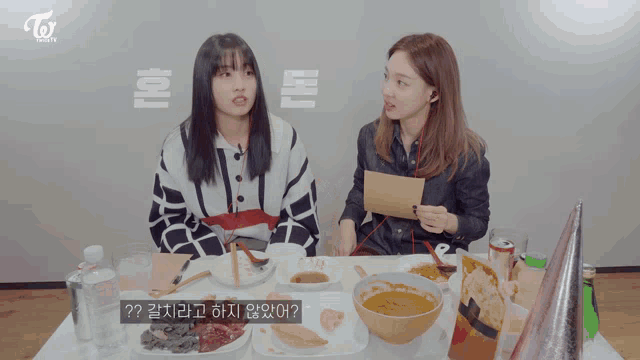 two girls sitting at a table with a twice logo on the bottom