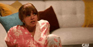a woman sits on a couch with a cw logo in the background