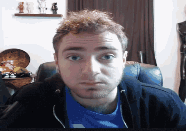 a man wearing a blue shirt and a black jacket is looking at the camera