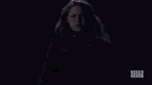 a woman stands next to a man in a dark room with the words show case on the bottom right