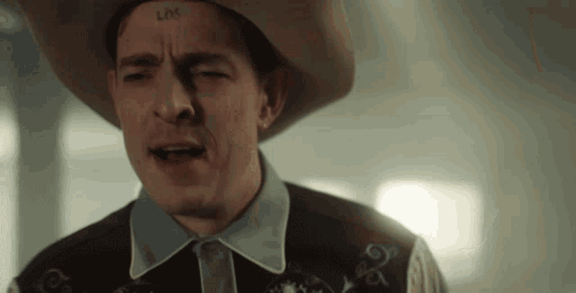 a man wearing a cowboy hat has a tattoo on his forehead that reads lxx