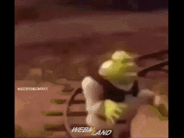 shrek is holding a tennis racket in a blurry image with webland written on the bottom right corner