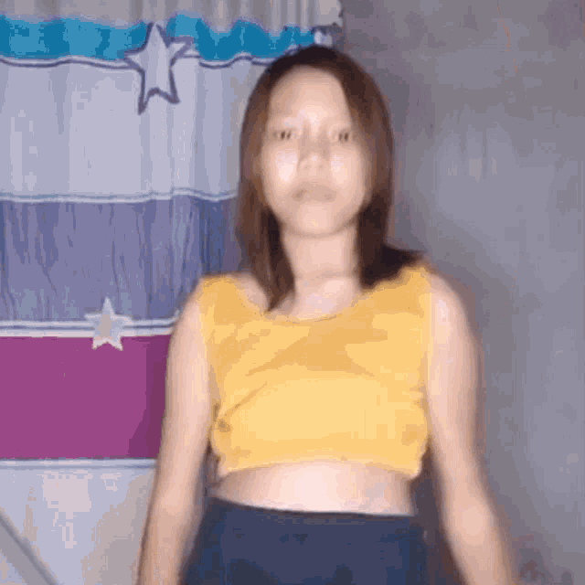 a young woman in a yellow crop top and blue skirt is standing in front of a curtain .
