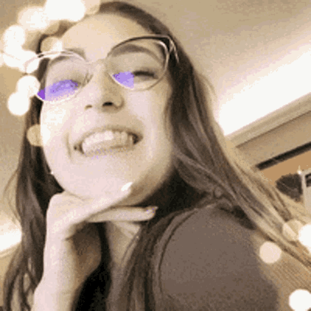 a woman wearing glasses is smiling with her hand on her chin .