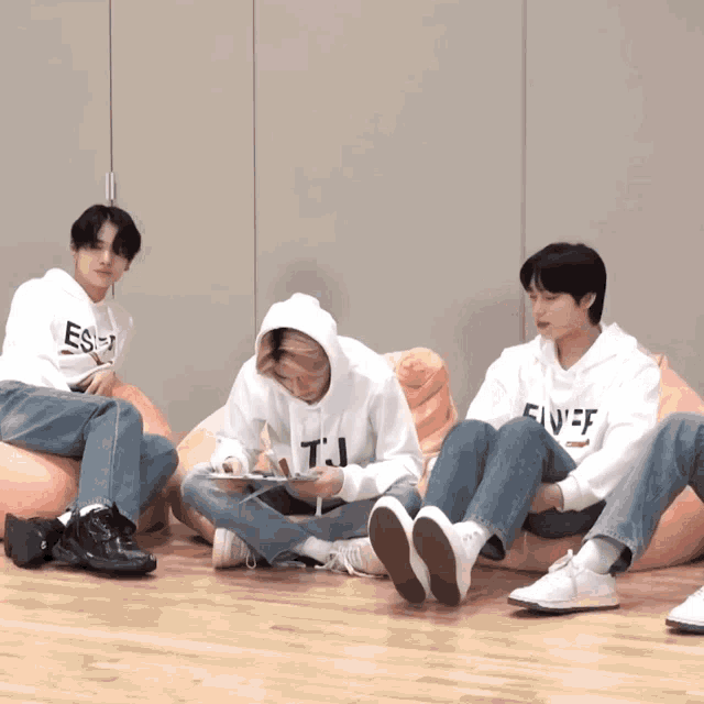 three young men are sitting on bean bag chairs and one of them is wearing a sweatshirt that says fivef