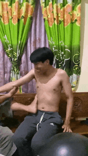a man without a shirt is sitting on a couch while another man massages his arm