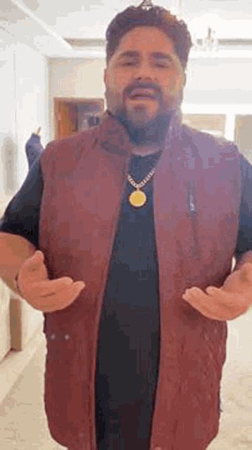 a man with a beard wearing a maroon vest and a gold necklace .