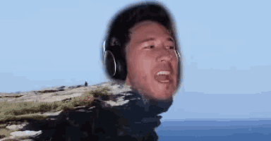 a man wearing headphones is standing on top of a rocky cliff .
