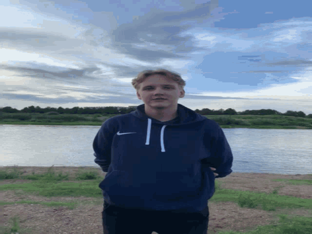 a man in a blue nike sweatshirt stands in front of a body of water