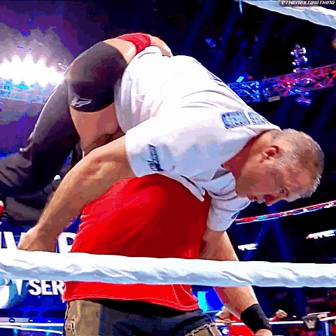 a wrestler in a white shirt with the word american on it is carrying another wrestler in a red shirt