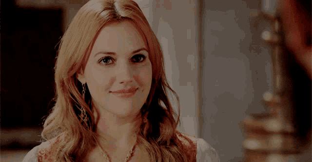 a woman with red hair and a gold necklace is smiling