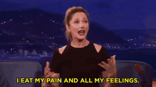 a woman is sitting on a couch with her hands on her chest and says `` i eat my pain and all my feelings '' .