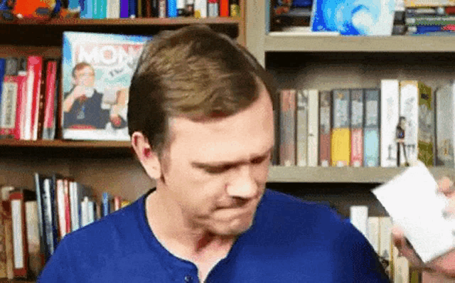 a man in a blue shirt is holding a remote control in front of a bookshelf with a magazine on it that says mom