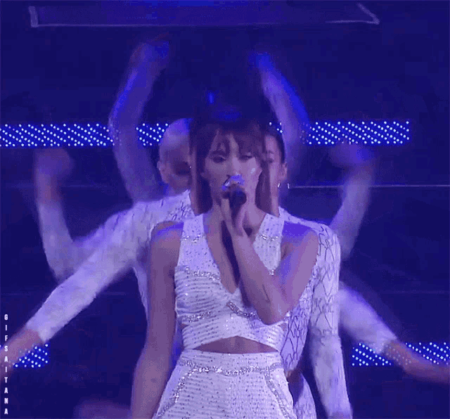 a woman in a white dress is singing into a microphone while dancing