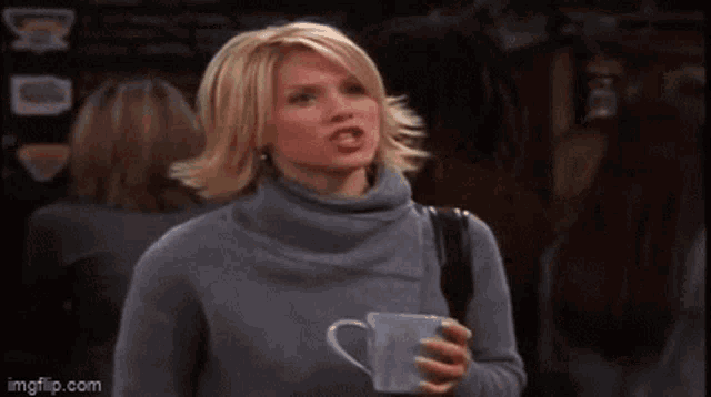 a woman in a gray sweater is standing in front of a crowd and says " okey " .
