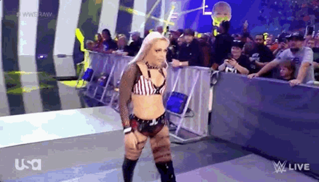 a female wrestler is walking down a ramp in front of a crowd during a wrestling match .