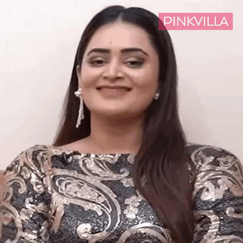 a woman wearing a sequined top and earrings smiles for the camera with a pinkvilla logo behind her