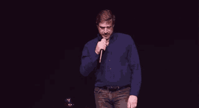 a man in a blue shirt is singing into a microphone on a stage