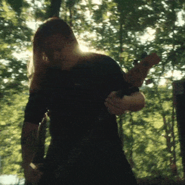 a man in a black shirt playing a guitar in the woods