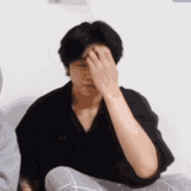 a man is sitting on the floor covering his face with his hand .