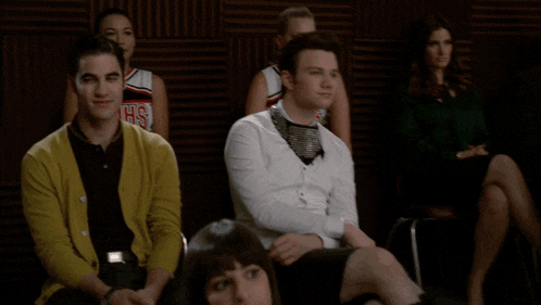 a man in a yellow cardigan sits next to a man in a white shirt with the word mmhs on his shirt