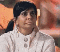 a woman is wearing a white sweater and earrings and looking at the camera .