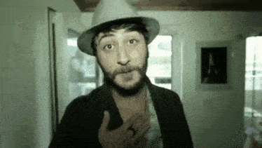 a man with a beard wearing a hat and a black jacket