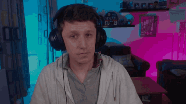a man wearing headphones looks at the camera in front of a shelf with a clock that says " sex "