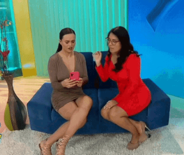 a woman in a red dress sits next to another woman on a blue couch