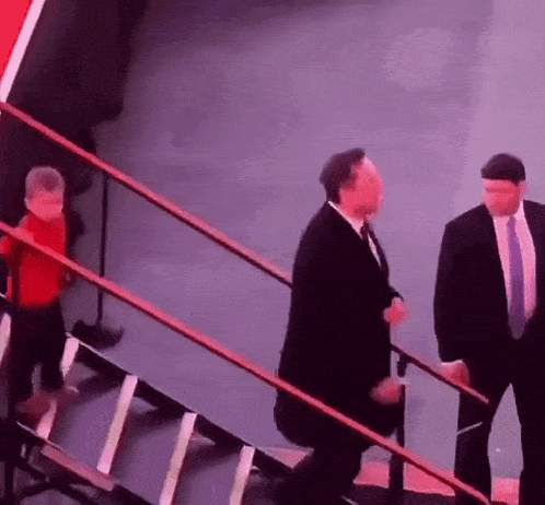 a man in a suit and tie is walking down a set of stairs with a child in a red shirt behind him