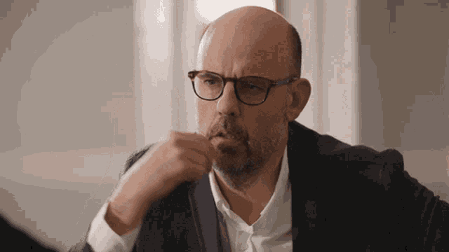 a bald man with glasses and a beard looks serious