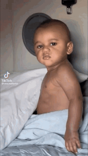 a baby without a shirt is laying on a bed and looking at the camera