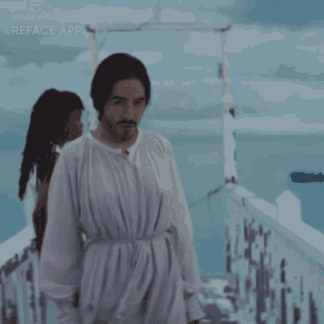 a man in a white robe is standing on a bridge with a woman behind him