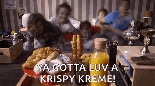 a group of people are sitting around a table with a tray of food and a bottle of orange juice .