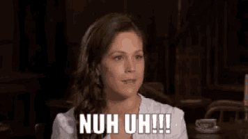 a woman is smiling and sitting at a table with the words nuh uh !!! written on her face .