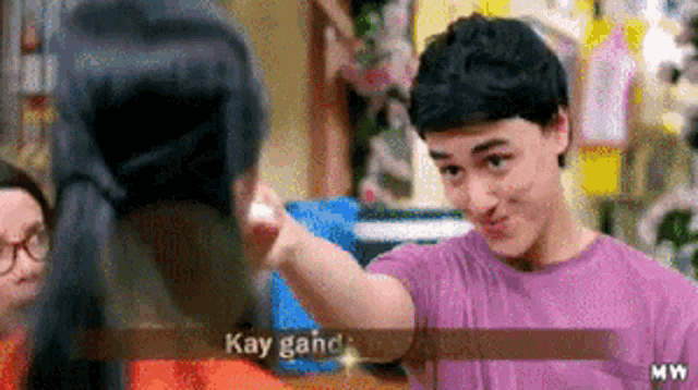 a man in a purple shirt is talking to a woman in a room with kay ganda written on the screen .