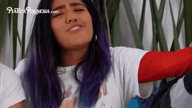 a woman with purple hair is wearing a white t-shirt and a red sleeve .