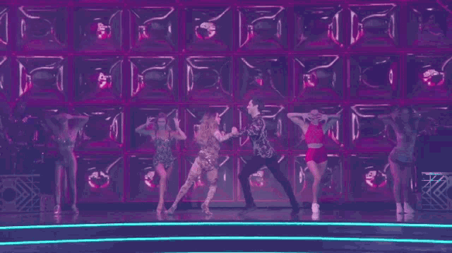 a group of people are dancing in front of a purple wall