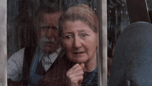 a man and a woman are looking out a window and the woman is pointing
