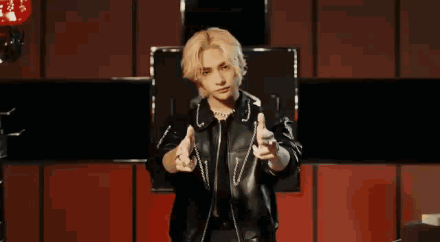 a man in a leather jacket is standing in front of a red wall .