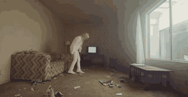a man in a white suit is standing in a living room with a couch .