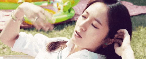 a woman is laying on a blanket in the grass with her eyes closed and holding her hair .